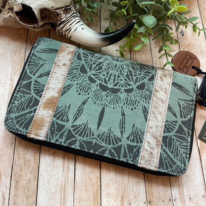 Green patterned pouch with a decorative horn and plant on a wooden surface