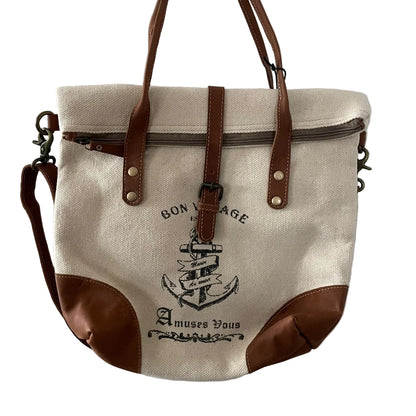 Canvas tote bag with brown leather straps and accents, featuring an anchor design, hanging on a white door.