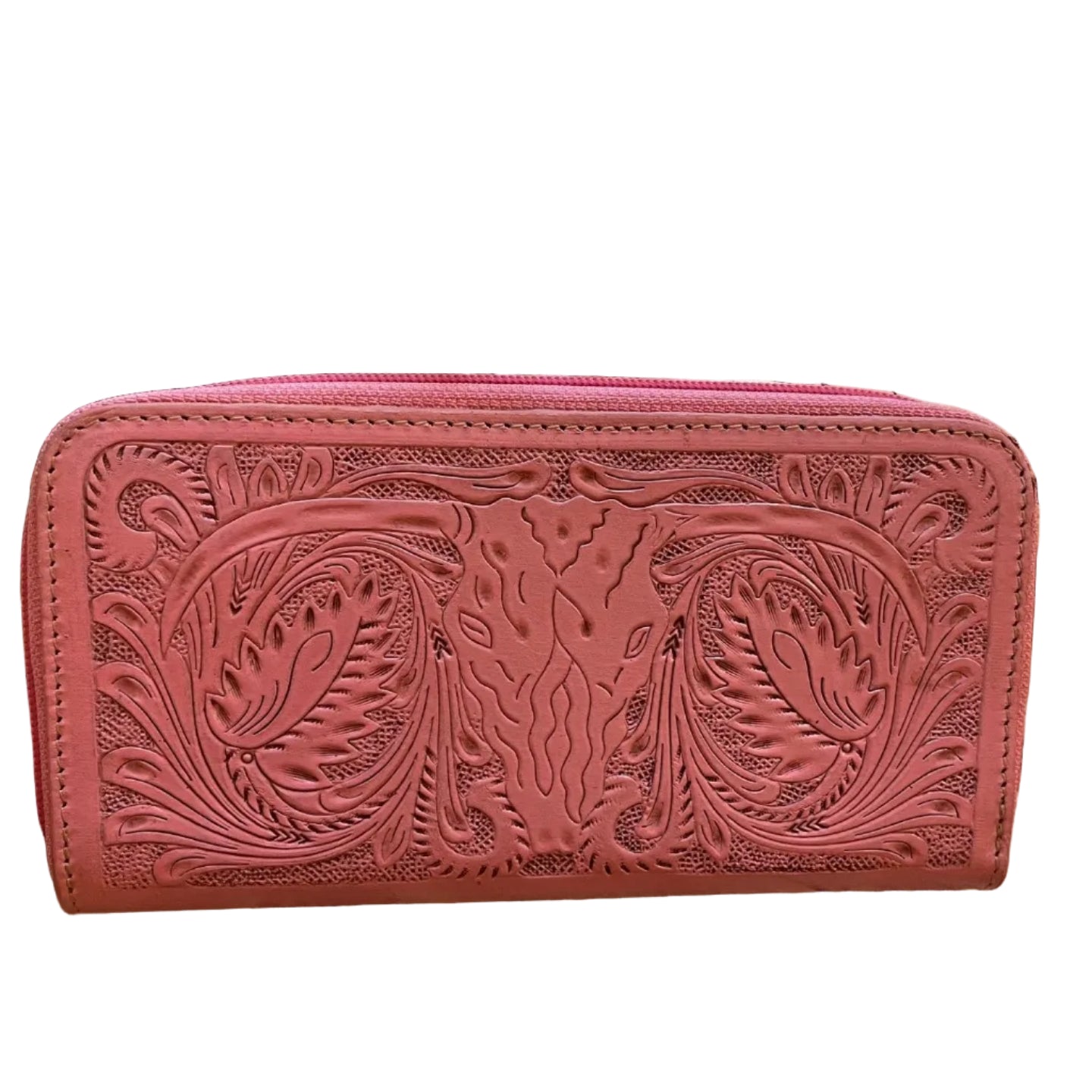 Pink leather wallet with intricate patterns on a wooden surface with plants in the background