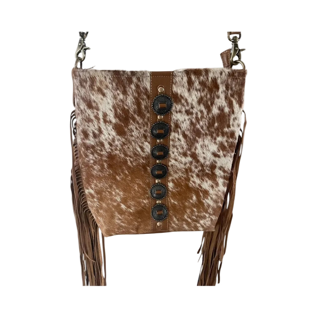 Brown and white cowhide bag with black buttons and fringes on a white background