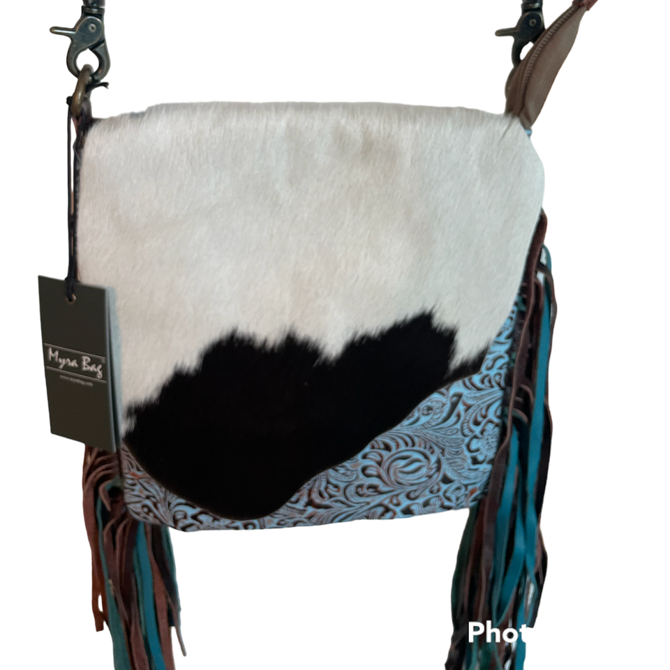Cowhide leather crossbody bag with patterned flap and fringes on a white background