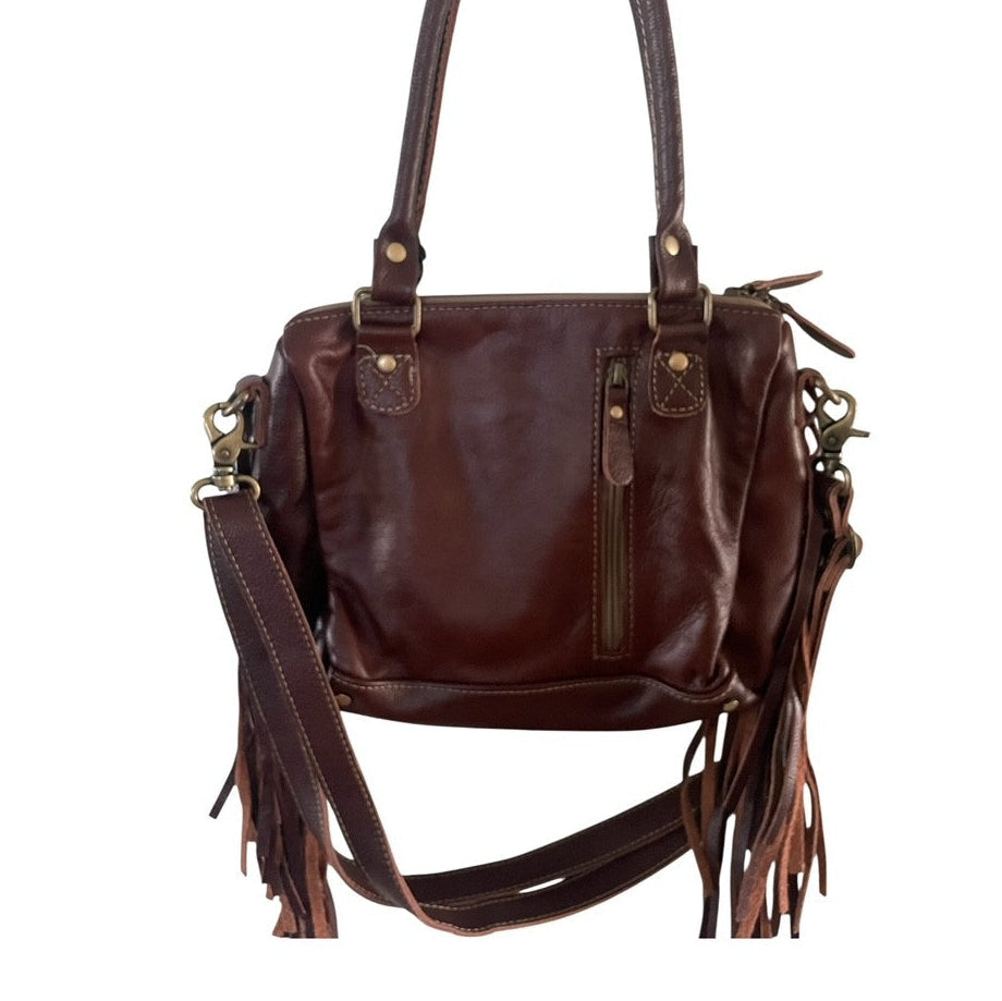 Brown leather handbag with fringe details and a zippered concealed carry area on a white background