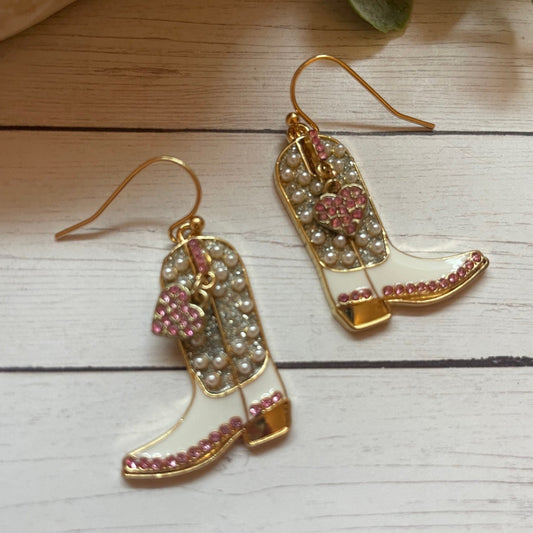 Pair of gold earrings with pink hearts and pearl details on a wooden surface.