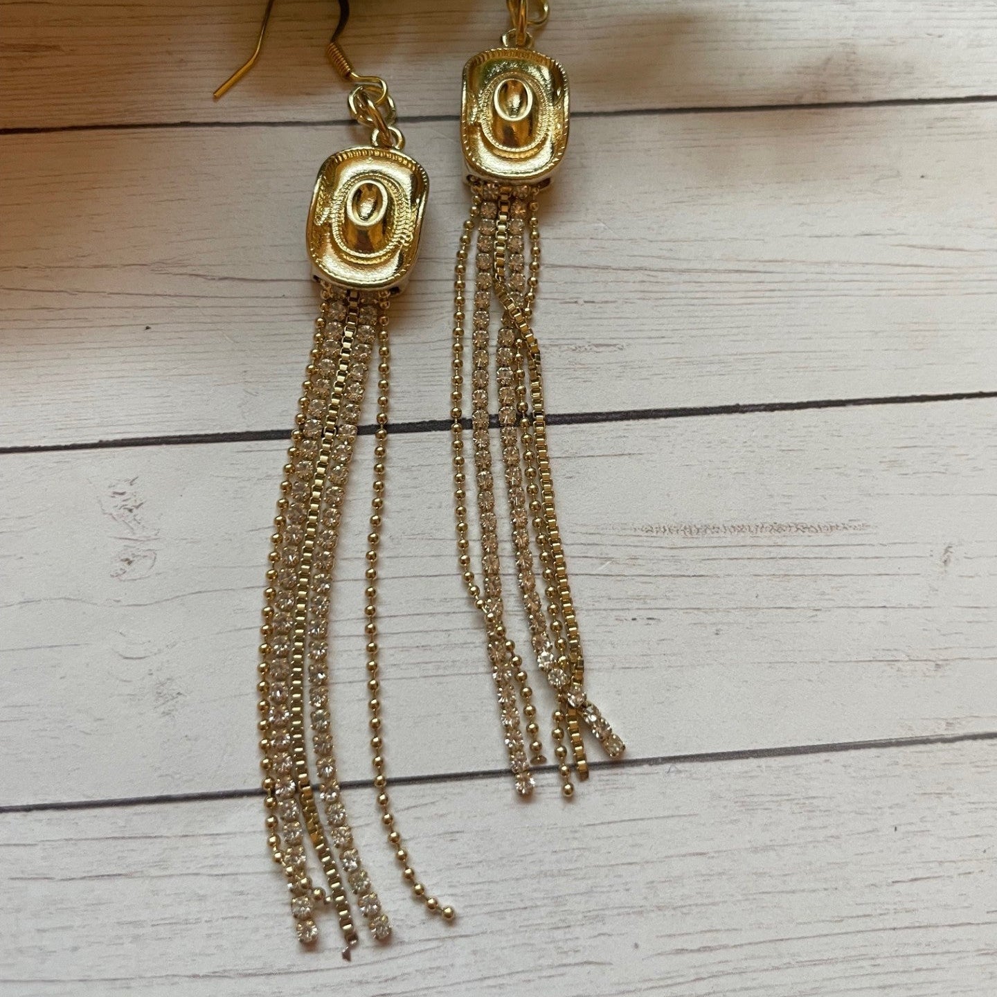 Gold tassel earrings on a wooden surface with green leaves.