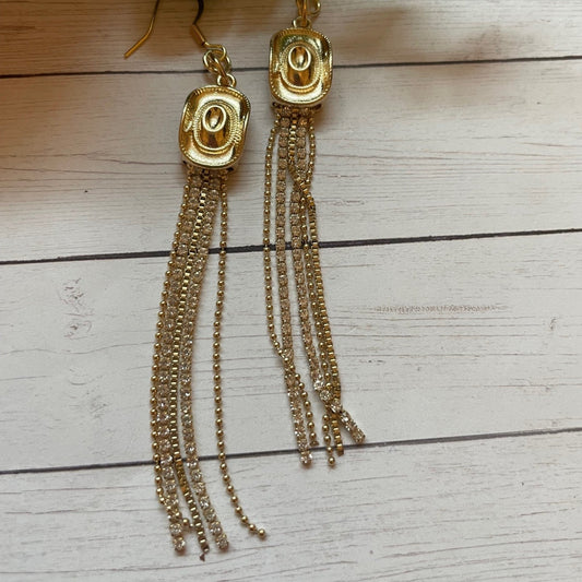 Gold tassel earrings on a wooden surface with green leaves.