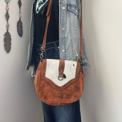 Mannequin wearing a denim jacket, black shirt, and blue jeans with a brown and white leather bag against a neutral background.