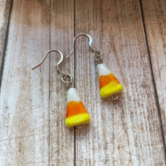 Candy corn dangle earrings with silver fishhook wires, displayed on a rustic wooden surface with a piece of driftwood at the top.