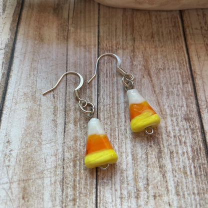 Candy corn dangle earrings with silver fishhook wires, featuring white, orange, and yellow striped beads on a rustic wooden surface.