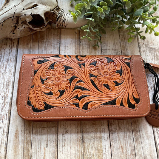 Brown leather wallet with floral tooling on a wooden surface with a skull and plant in the background