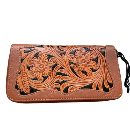 Brown leather wallet with floral tooling on a wooden surface with a skull and plant in the background