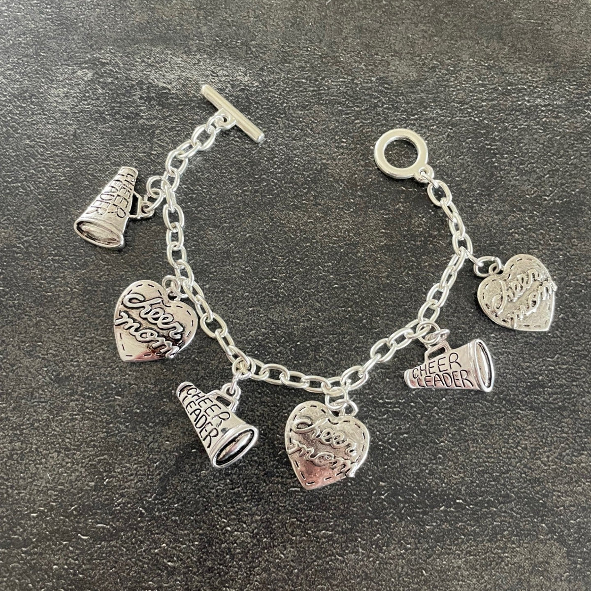 silver cheerleading charms on a silver toggle bracelet with a black grey background
