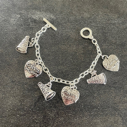 silver cheerleading charms on a silver toggle bracelet with a black grey background