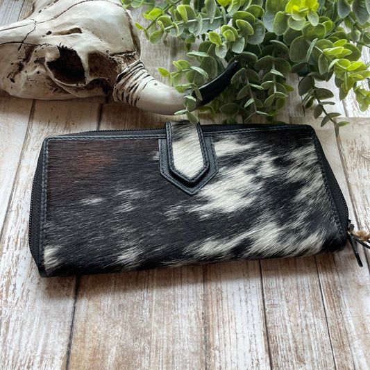 Black and white cowhide wallet on a wooden surface with a skull and plant in the background
