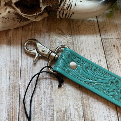 Turquoise leather keychain with floral patterns on a wooden surface