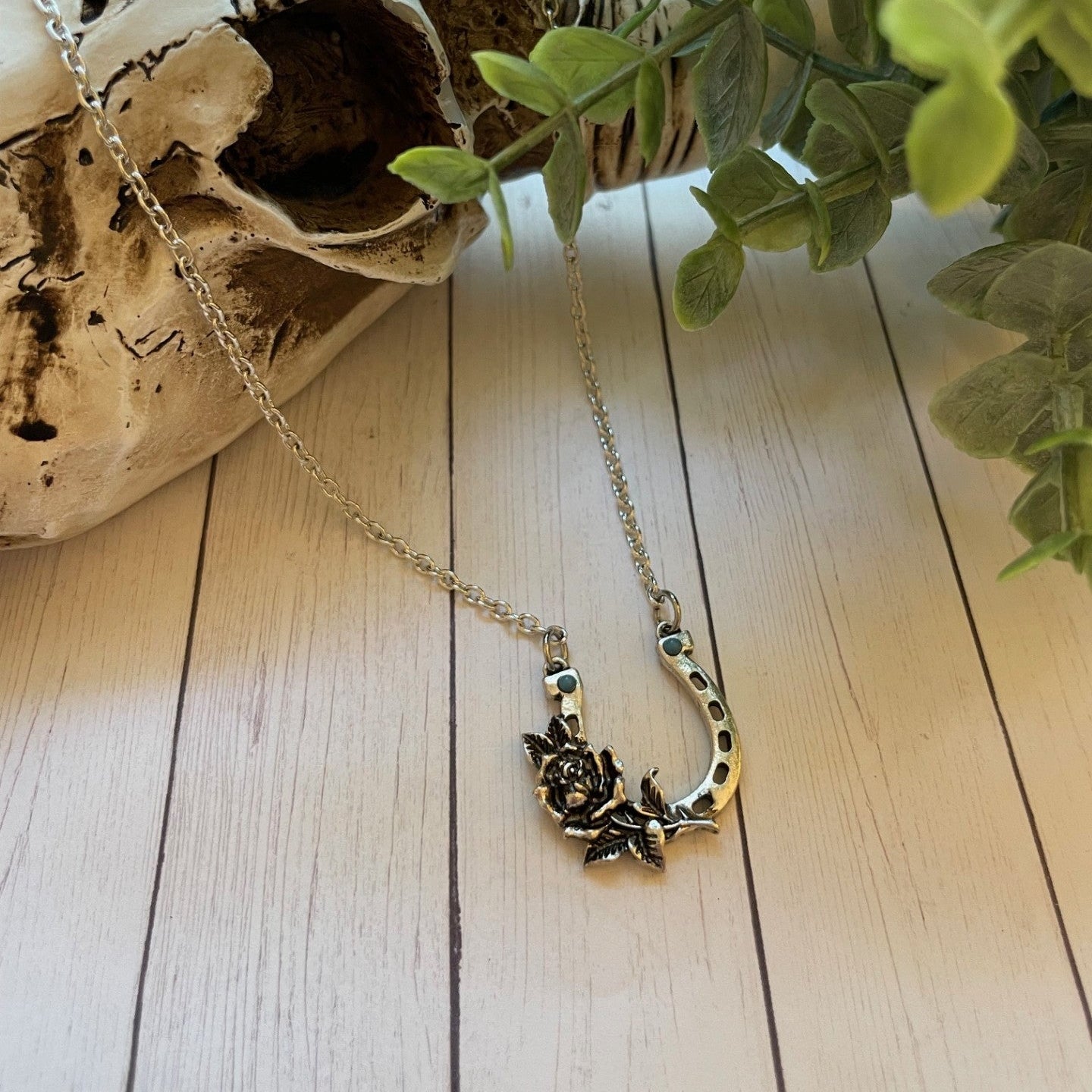 Necklace with a floral horseshoe pendant on a wooden surface with a skull and plant in the background