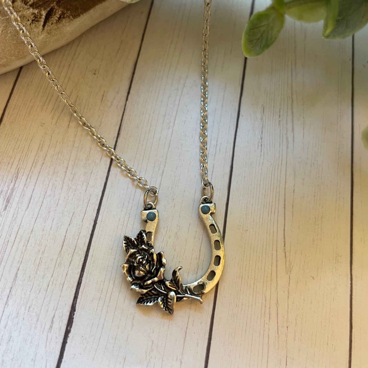 Silver necklace with a horseshoe and floral pendant on a wooden surface