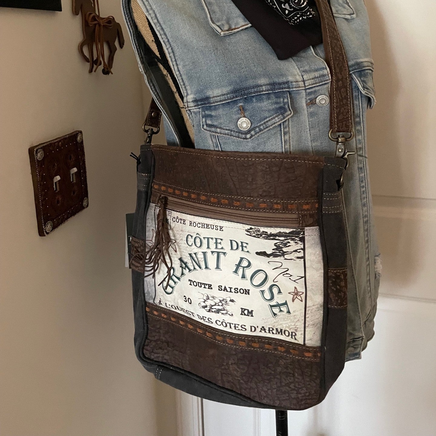 Brown leather bag with text on a mannequin against a neutral wall.
