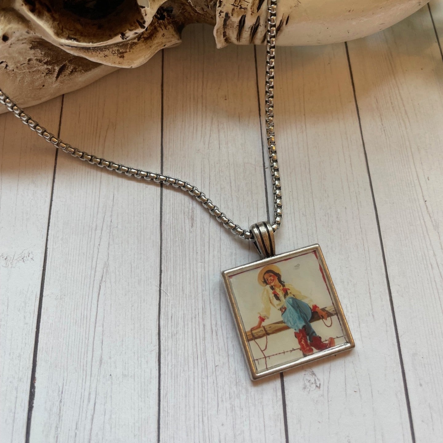 Silver necklace with a square vintage cowgirl type print on a wood background 