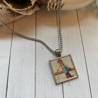 Silver necklace with a square vintage cowgirl type print on a wood background 