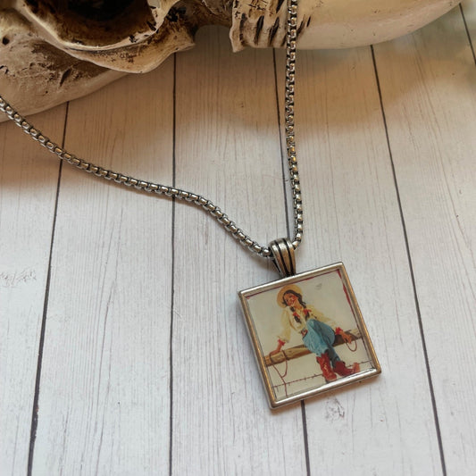 Silver necklace with a square vintage cowgirl type print on a wood background 