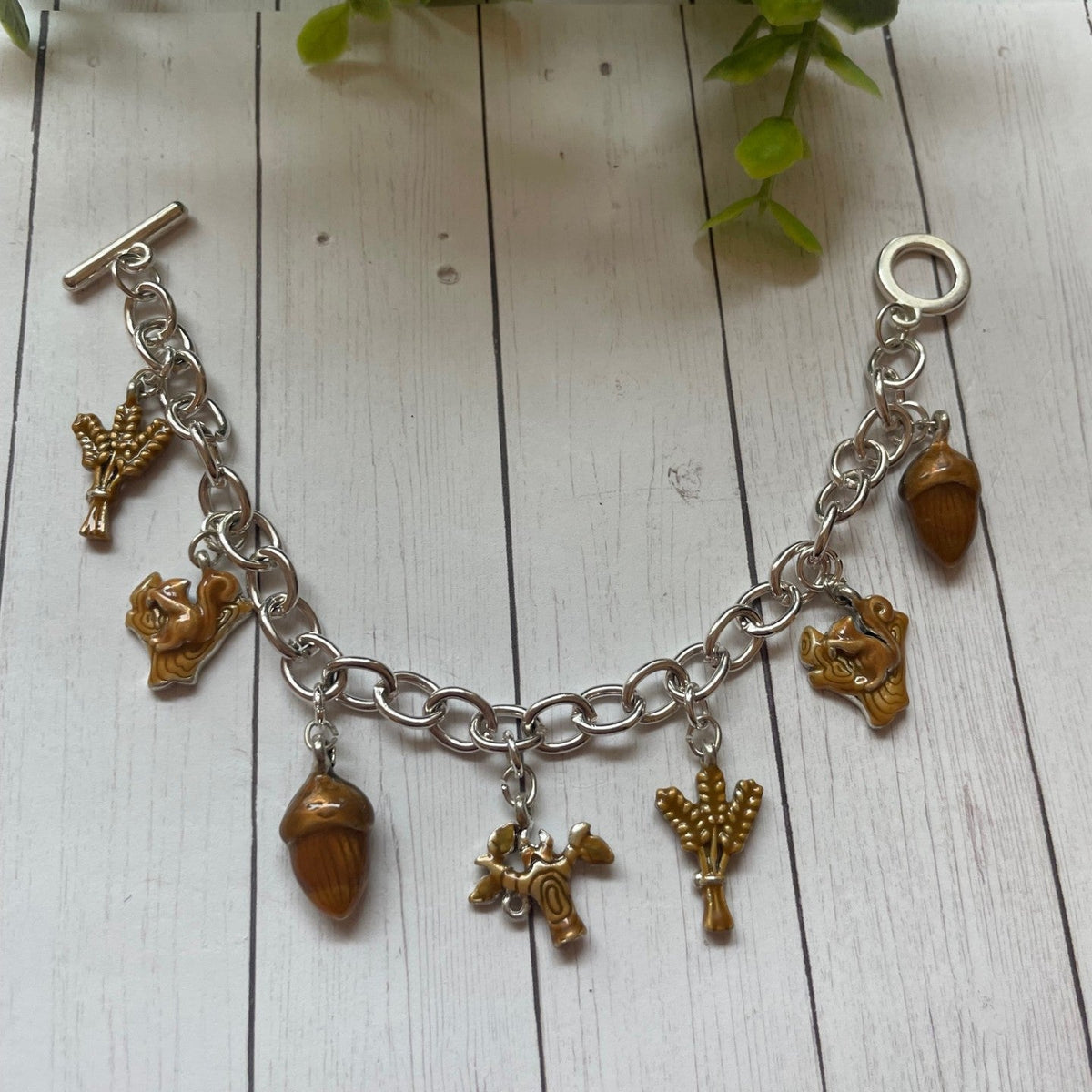 Fall and autumn brown charms on a silver toggle bracelet, acorn squirrel wheat charms on a white wood background