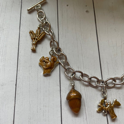 Fall and autumn brown charms on a silver toggle bracelet, acorn squirrel wheat charms on a white wood background