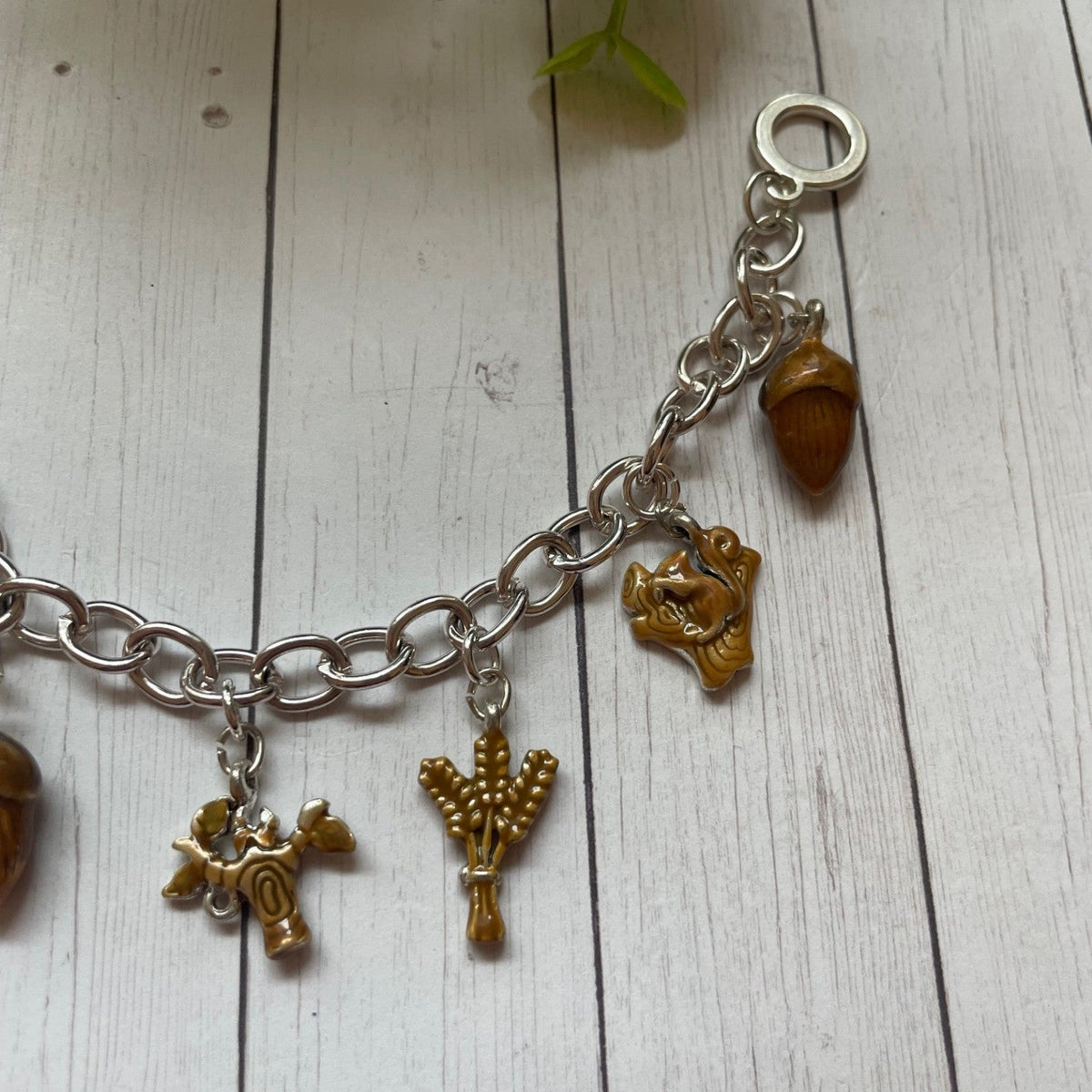Fall and autumn brown charms on a silver toggle bracelet, acorn squirrel wheat charms on a white wood background