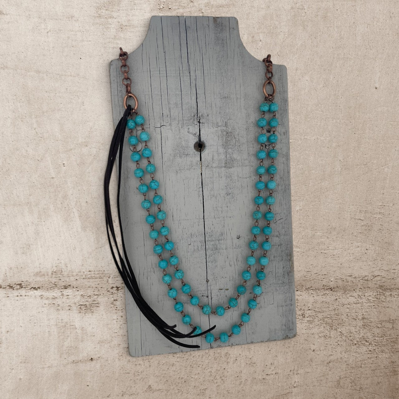 Turquoise beaded necklace with black accents on a wooden stand against a textured beige background