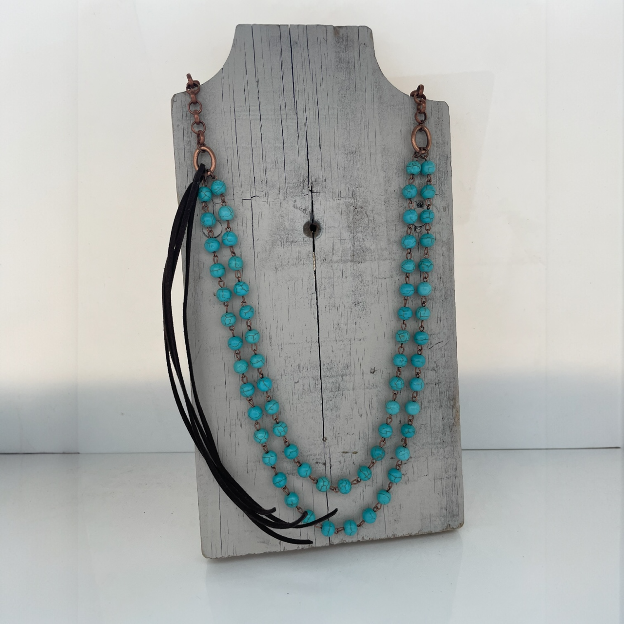 Turquoise beaded necklace with black accents on a wooden stand against a white background