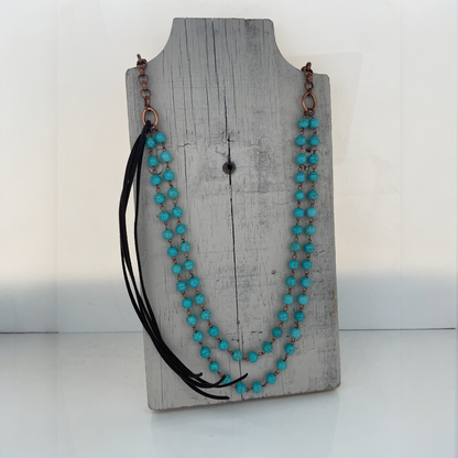 Turquoise beaded necklace with black accents on a wooden stand against a white background