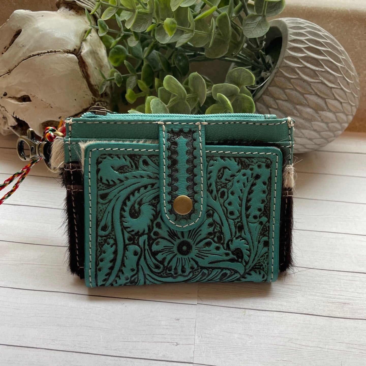 Turquoise leather wallet with intricate designs on a wooden surface with a plant in the background