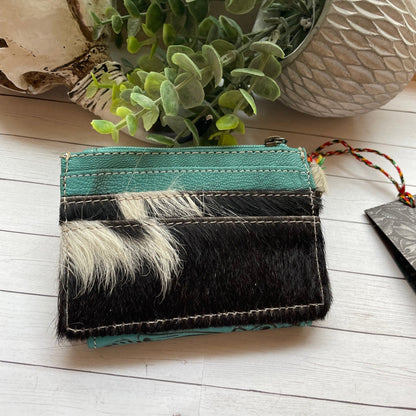 Small wallet with black and white fur pattern on a light wooden surface with plants in the background