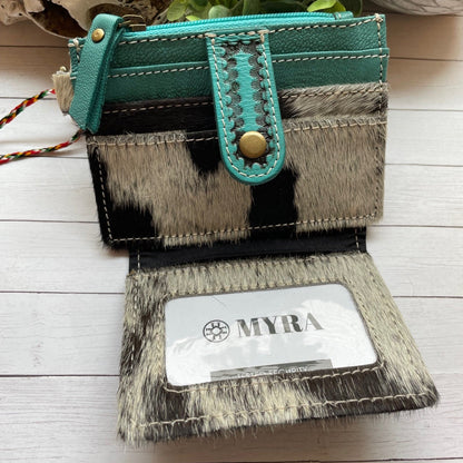 Teal and cowhide patterned wallet with 'MYRA' branding on a light wooden surface.