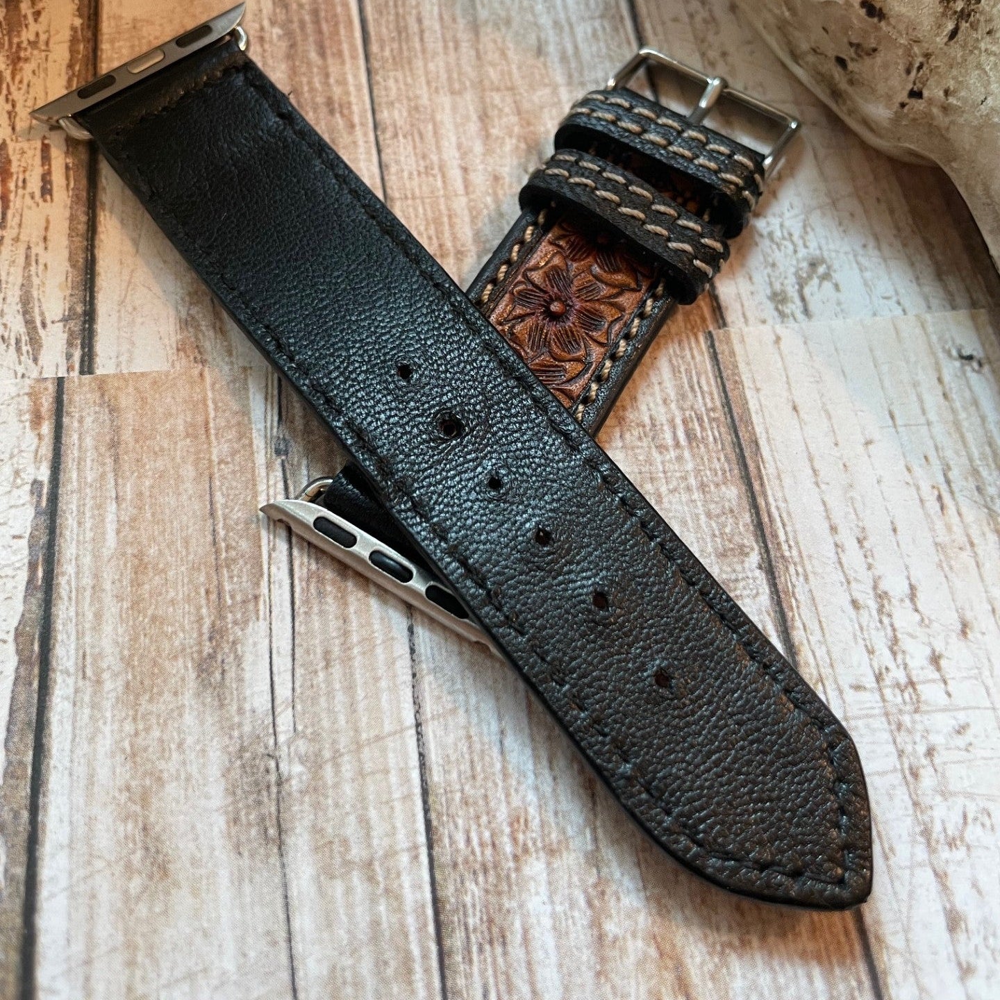 Black leather watch strap with metal clasp on a wooden surface