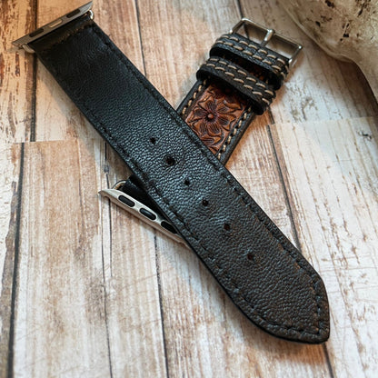 Black leather watch strap with metal clasp on a wooden surface
