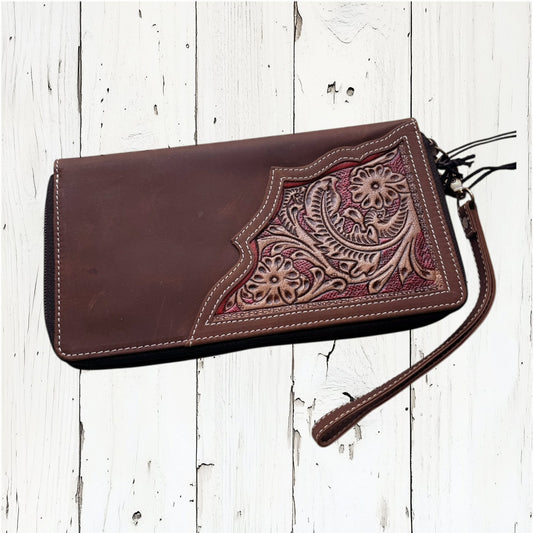 Brown leather clutch with intricate floral embossing on a white wooden surface