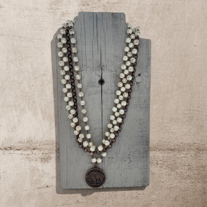 Necklace with white beads and a brown pendant on a wooden board