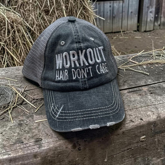 Black cap with 'Workout Hair Don't Care' text on a wooden surface with hay in the background